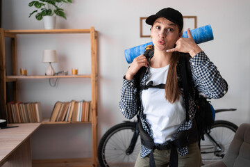 shocked woman going on a hiking trip with backpack showing phone call me gesture looking at camera...