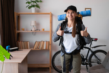 portrait of female hiker traveler with backpack showing thumbs up ready to travel at home. Looking...