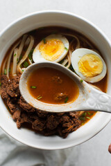 Overhead view of spicy broth for noodles, top view of spicy pepper broth in a ceramic spoon