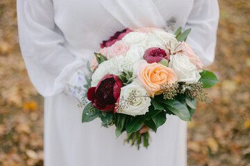 Beautiful bridal bouquet held by a woman in a white dress during an outdoor autumn wedding ceremony