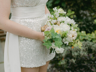 Beautiful wedding bouquet held by bride in sparkling dress surrounded by nature during outdoor...