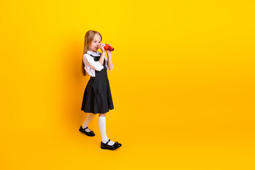 Portrait of a charming young girl holding binoculars against a vibrant yellow background
