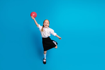Cheerful schoolgirl playing with a red balloon in a uniform against a blue background