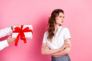 Displeased young woman crossing arms, rejecting gift box in front of pink background, revealing...