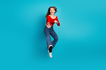 Cheerful young woman in casual style jumping on blue background expressing excitement and enjoying...