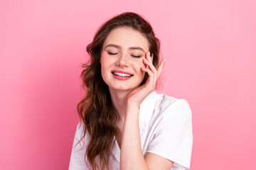 Charming young woman with brown hair smiling gently on a pink background dressed in elegant casual...