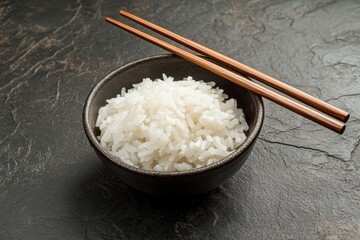 Cooked white rice served in a black bowl with wooden chopsticks on a dark surface