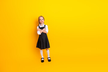 Cheerful young student girl in a school uniform posing on a vibrant yellow background with style...