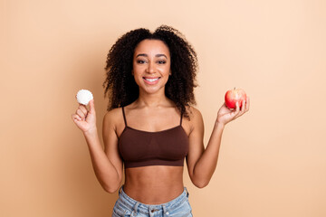 Young Woman Smiling Cheerfully Holding an Apple and a Small Shell Against a Beige Background