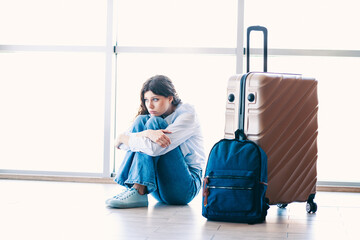Charming woman sitting with luggage at an airport terminal in casual attire, evoking feelings of...