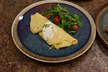 A freshly served omelette with arugula and cherry tomato salad on a rustic ceramic plate