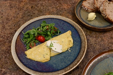 A freshly served omelette with arugula and cherry tomato salad on a rustic ceramic plate