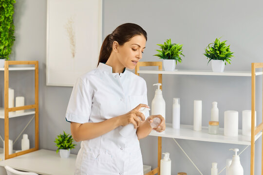 Young smiling woman cosmetologist standing in beauty spa salon on her workplace and applying moisturizing cream or lotion on hand. Cosmetology, wellness, body and skin care concept