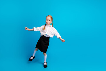 Smiling young girl in school uniform enjoying a playful moment against a vibrant blue background, radiating happiness