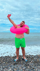 Vertical mobile photo. Mature tanned fat white man with big belly, green shorts, blue flip-flops,...