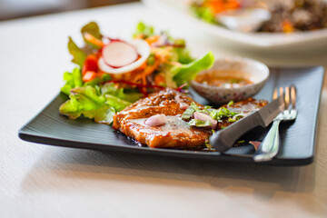 grilled pork steaks in black plate with spices at restaurant