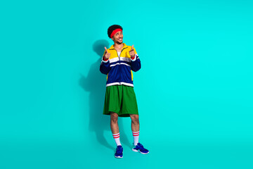 Energetic young man in retro sports outfit gives thumbs up on turquoise background representing...