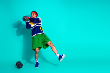 Young man exercising with weights in retro activewear on a vibrant turquoise background, embodying...