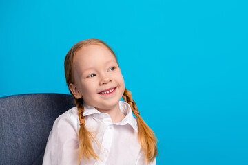 Smiling girl with red hair in braids wearing a white shirt against a bright blue background, posing...