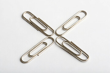Four metallic paper clips arranged in a cross shape on a clean white background