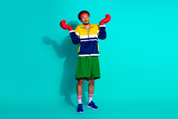 Energetic young man in vibrant sporty outfit posing playfully against a turquoise backdrop, exuding...