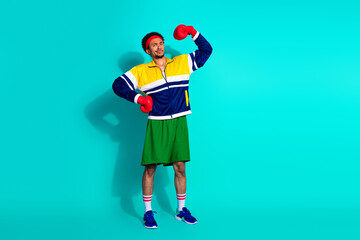 Athletic young man posing confidently in retro sportswear and boxing gloves against a teal...