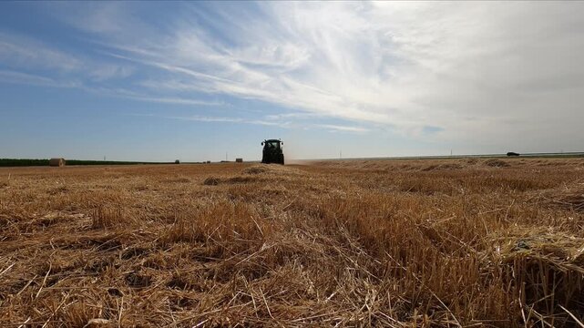 A tractor with a baler attached to it working in a field during harvesting