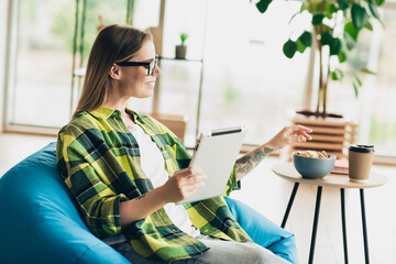 Young woman relaxing on a beanbag while using a digital tablet in a stylish bright room with casual...