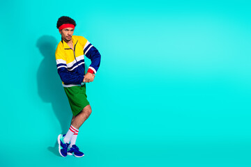 Obraz premium Young male athlete in retro outfit practicing a dynamic pose against a vibrant turquoise background showcasing vintage sporty fashion.
