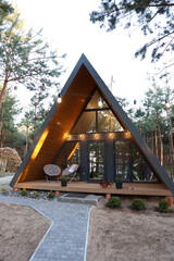 Modern A-frame cabin in a pine forest with hammock, trampoline, and string lights. Peaceful woodland retreat with cozy outdoor vibes