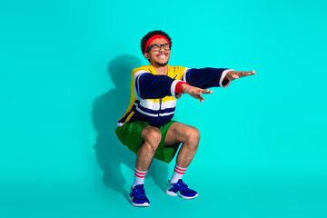 Young athletic man in vibrant retro sportswear performing fitness exercises against a bright teal background