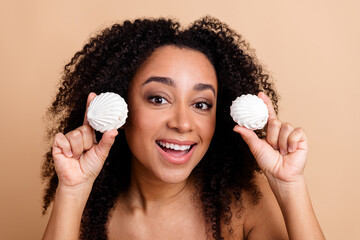 Cheerful young woman holding decorative items while showcasing curly hair on a beige background