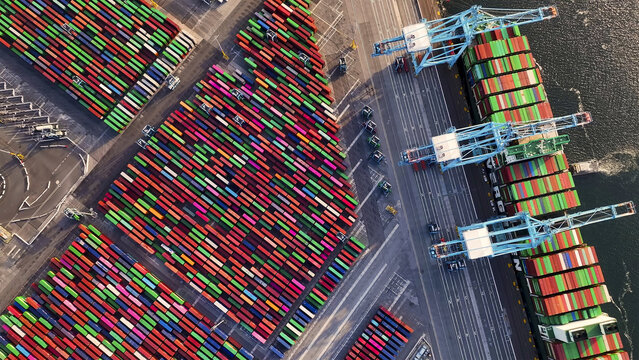 Port of Oakland, United States - 07 April 2025: Aerial view of a vast, colorful mosaic of stacked containers meets the steely blues of cranes and the dark, reflective waters of the harbor.