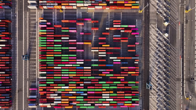 Port of Oakland, United States - 07 April 2025: Aerial view of vibrant, stacked shipping containers casting long shadows, creating a geometric tapestry of commerce and industry.