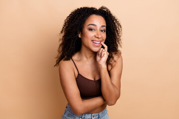 Smiling young woman with curly hair standing confidently against a beige background showcasing...
