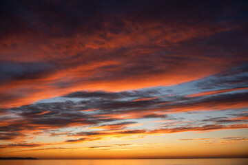 Vibrant sunset sky with dramatic clouds in shades of orange, pink, and purple reflecting over calm...