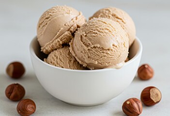 Close-up of a white bowl filled with three scoops of hazelnut creamy ice cream, garnished with a hazelnuts