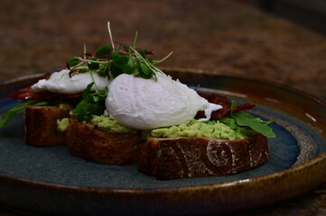 Delicious open-faced sandwich served on rustic bread with mashed avocado, crispy bacon, perfectly poached eggs and a topping of fresh microgreens.