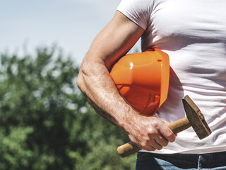 Attractive man, hammer hard hat and work clothes. Labor day. Front view, close-up. Sunny day, Labor and employment concept