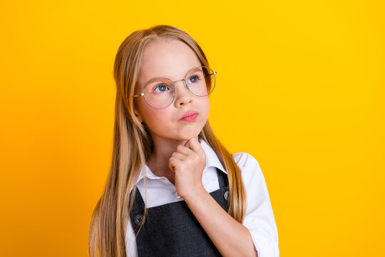 Thoughtful young schoolgirl wearing glasses on a vibrant yellow background for education and academic concepts - Powered by Adobe