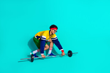 Retro styled man lifting weights in vibrant activewear against turquoise background showcasing...