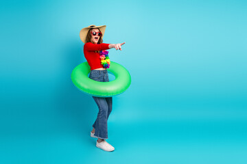 Stylish and cheerful young woman in casual wear posing with green inflatable ring against bright...