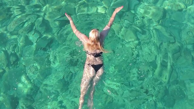Beautiful Young Woman in Bikini Swims in Stara Baska Beach Krk Island, Croatia. Mediterranean Summer. Aerial Shot From Above. Blue Sea the Rocks  Mountains and Coastline Calm Sea With Clear Blue Water