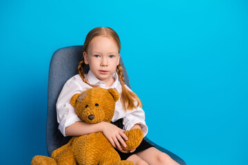 Adorable young girl holding a teddy bear against a blue background, symbolizing childhood innocence
