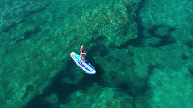 Beautiful Young Woman in Bikini Stand Up Paddling, Sup Surfing in Stara Baska Beach Krk Island, Croatia. Mediterranean Summer. Aerial Shot From Above. Blue Sea the Rocks  Mountains and Coastline