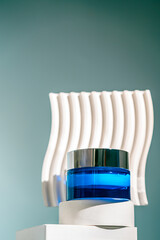 A blue glass jar of revitalizing face night cream with a silver lid is placed on a white pedestal,...