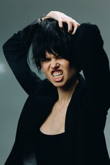 angry woman with short black hair expressing frustration and tension in black clothing on a gray...