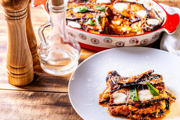 Eggplants alla parmesano on a white plate on a wooden table with a white napkin. Baked eggplants with tomatoes and cheese according to a traditional Italian recipe. High quality photo