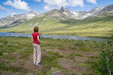 Woman enjoying the view of the snow covered mountains and green valley and river in Tromso region. Norway