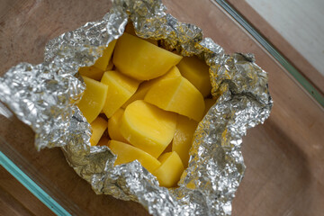 Top view of raw seasoned potatoes in foil ready for baking on a wooden table.
